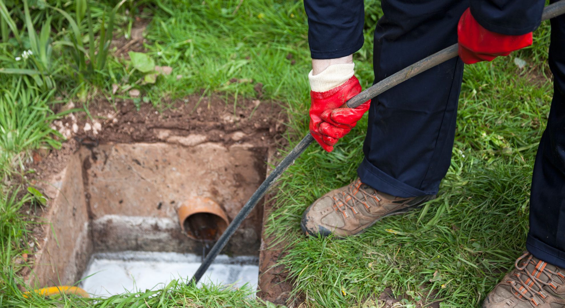 Man with ground open unblocking a drain with a tool